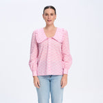 Woman wearing a pink blouse with a ruffled collar and light blue jeans on a white background